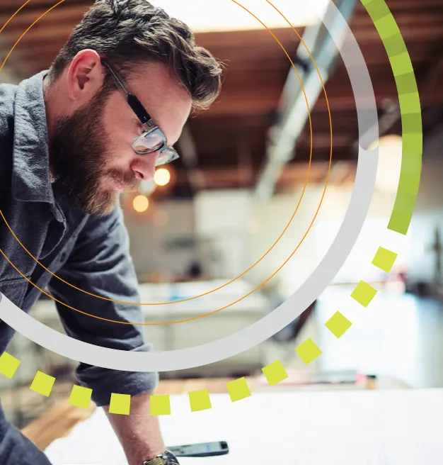 An AEC professional leans over a set of plans on a worktable, framed by RM ONE ring graphics