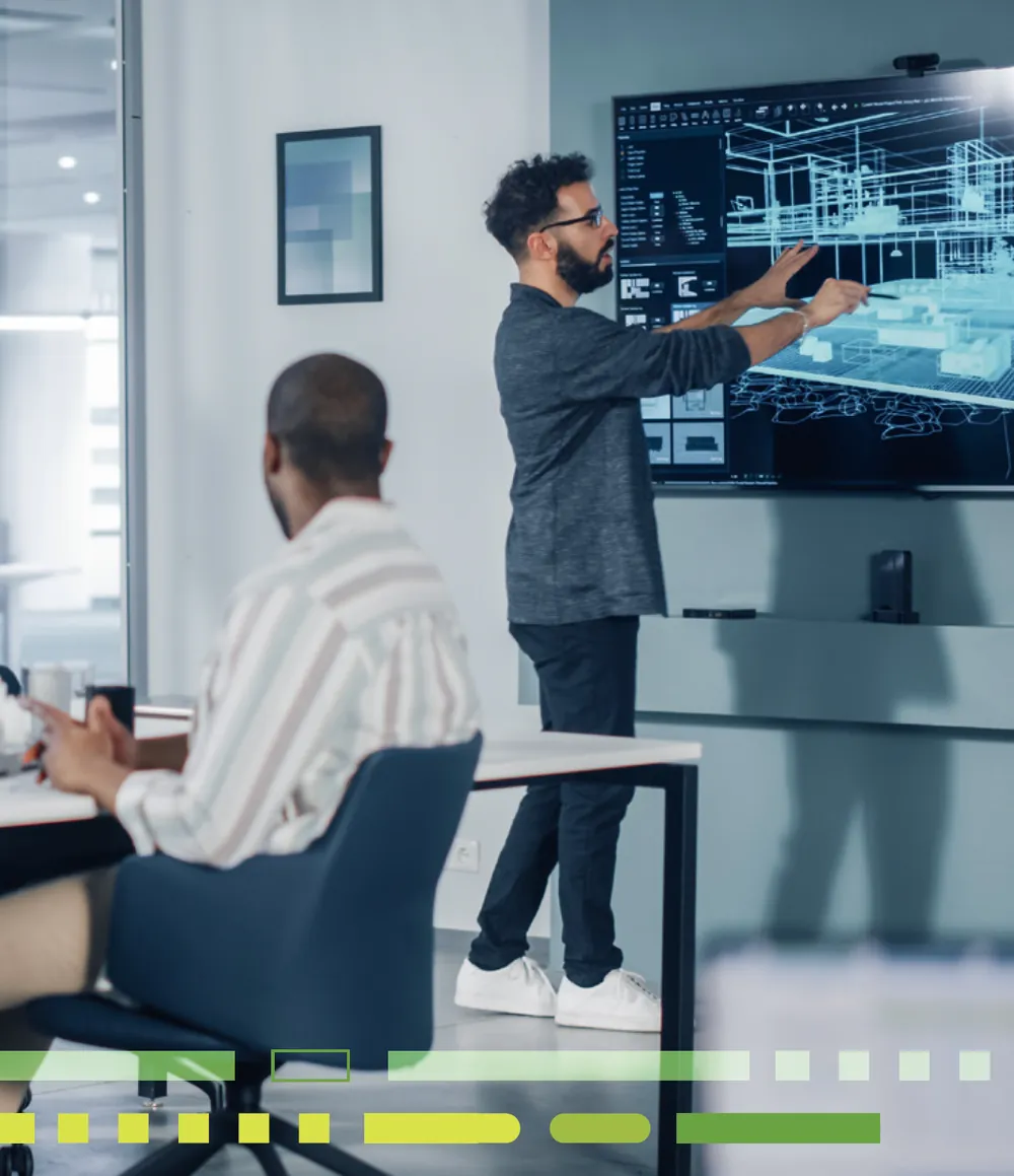 An operations leader reviews a project model on a large wall display while a colleague follows along